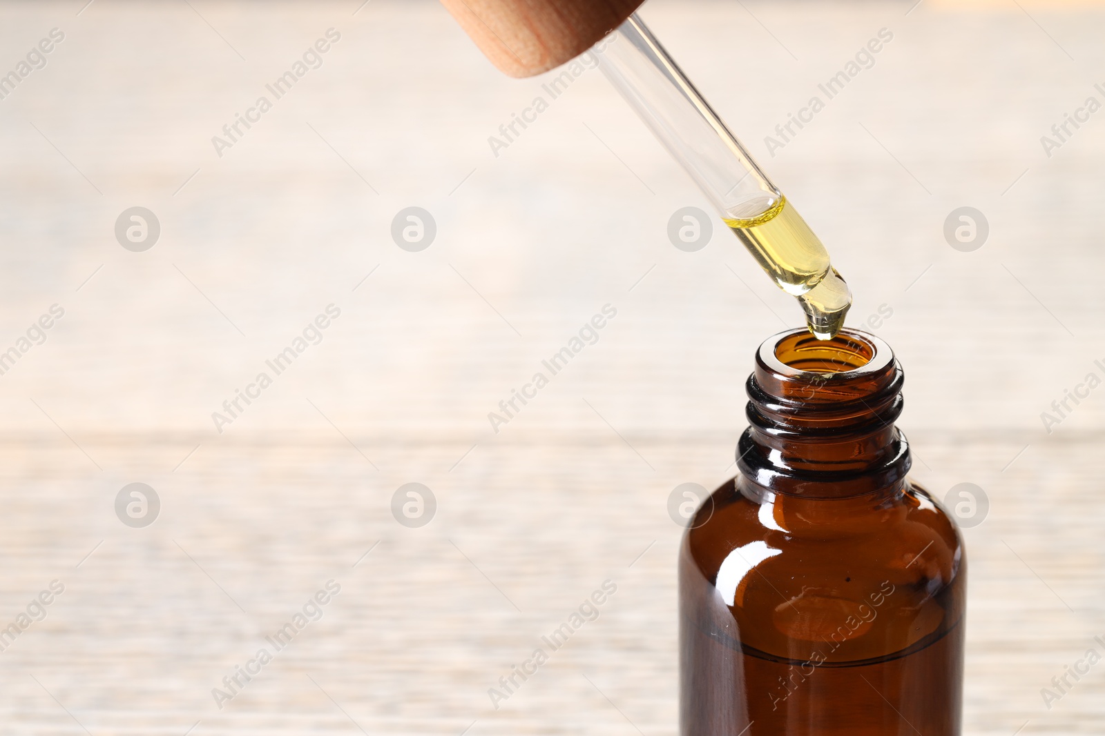 Photo of Essential oil dripping from pipette into bottle against blurred background, closeup. Space for text