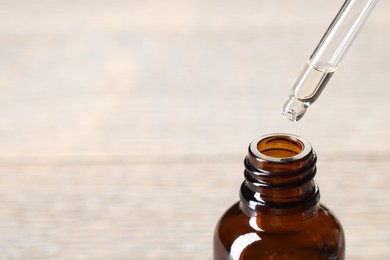 Photo of Essential oil dripping from pipette into bottle against blurred background, closeup. Space for text