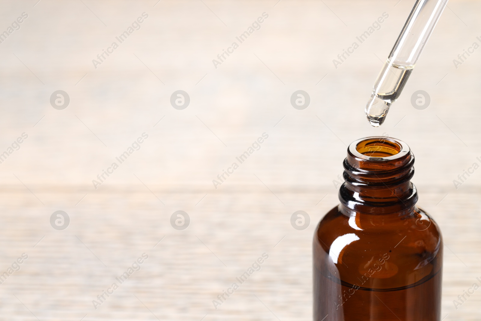 Photo of Essential oil dripping from pipette into bottle against blurred background, closeup. Space for text