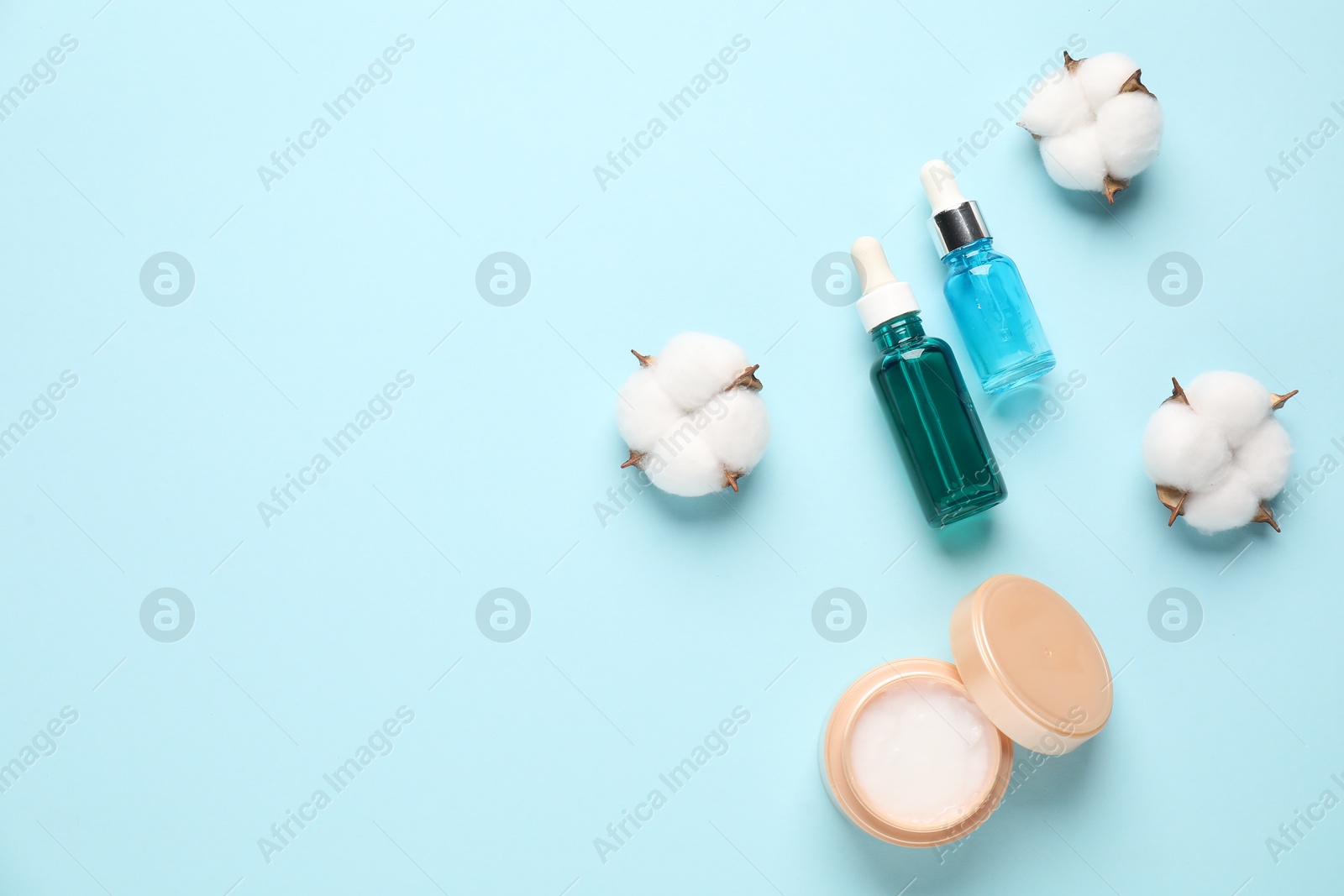 Photo of Different cosmetic products and cotton flowers on light blue background, flat lay. Space for text