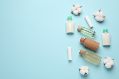 Photo of Different cosmetic products and cotton flowers on light blue background, flat lay. Space for text