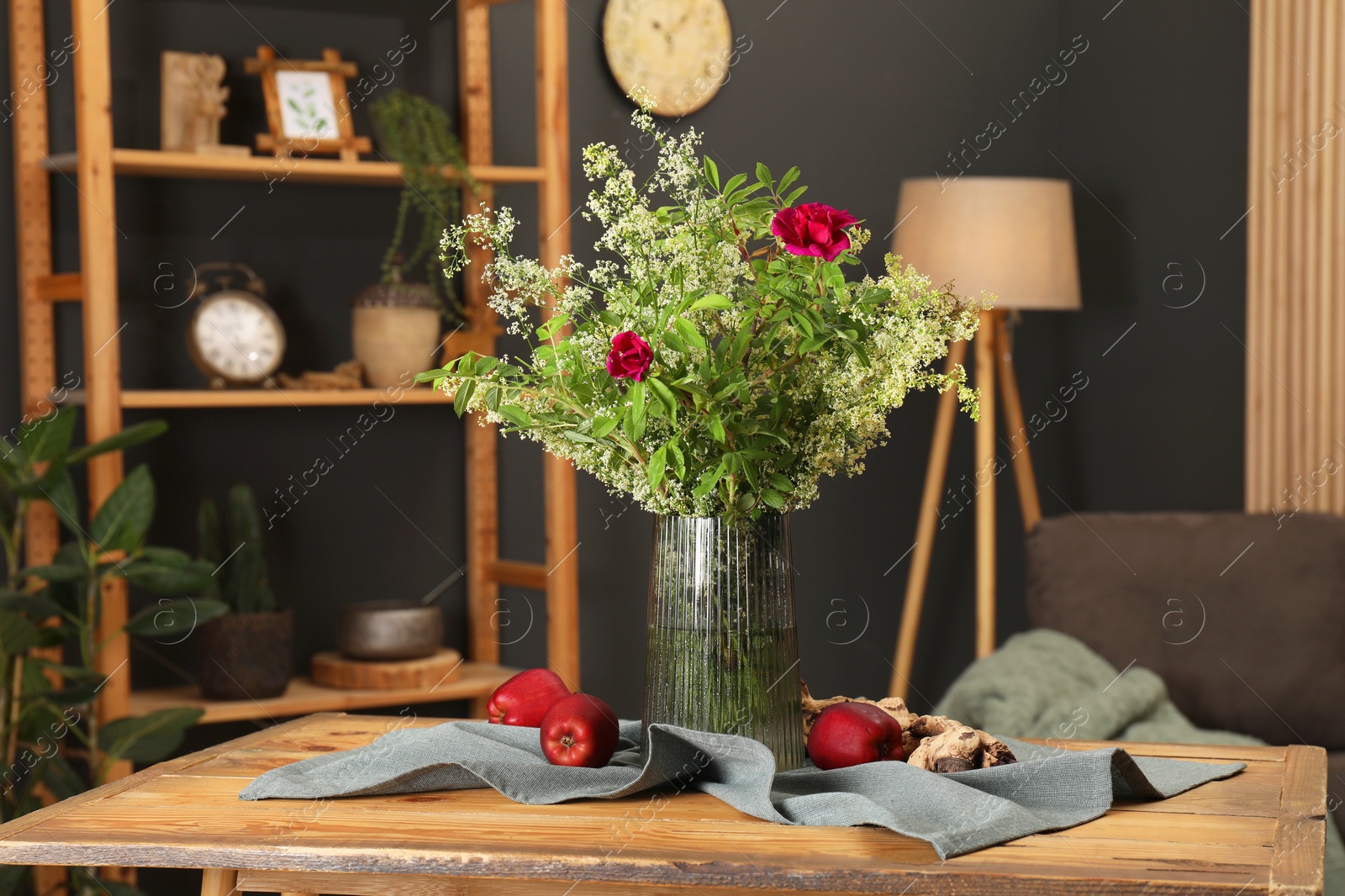 Photo of Ripe red apples and flowers on wooden table in stylish dining room