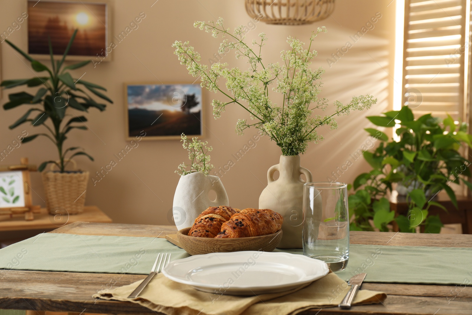 Photo of Clean tableware, flowers and fresh pastries on table in stylish dining room