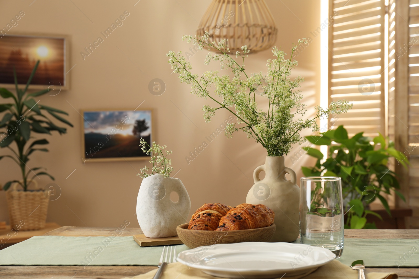 Photo of Clean tableware, flowers and fresh pastries on table in stylish dining room