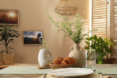 Clean tableware, flowers and fresh pastries on table in stylish dining room