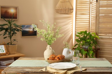 Photo of Clean tableware, flowers and fresh pastries on table in stylish dining room