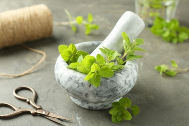 Photo of Mortar with sprigs of fresh green oregano and scissors on gray textured table, closeup