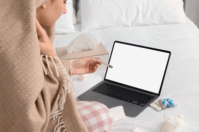 Sick woman with thermometer having online consultation with doctor via laptop at home