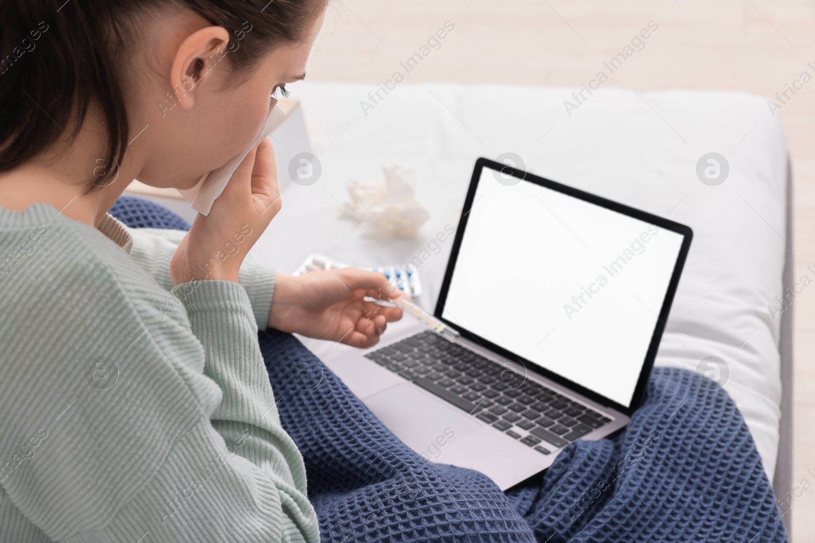 Photo of Sick woman with thermometer having online consultation with doctor via laptop at home