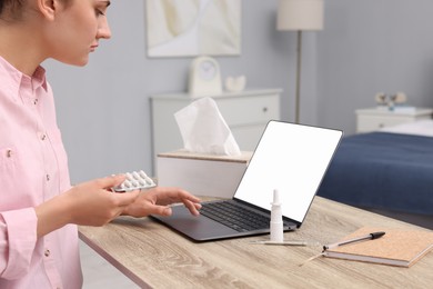 Photo of Sick woman with pills having online consultation with doctor via laptop at wooden table indoors