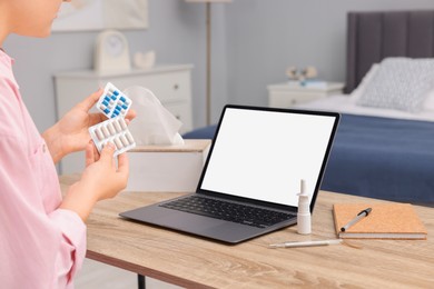 Sick woman with pills having online consultation with doctor via laptop at wooden table indoors