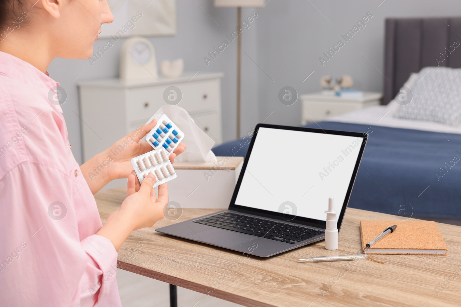 Photo of Sick woman with pills having online consultation with doctor via laptop at wooden table indoors