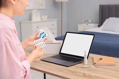 Photo of Sick woman with pills having online consultation with doctor via laptop at wooden table indoors