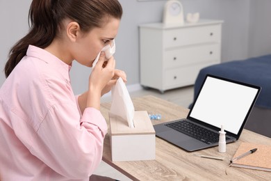 Sick woman having online consultation with doctor via laptop at wooden table indoors