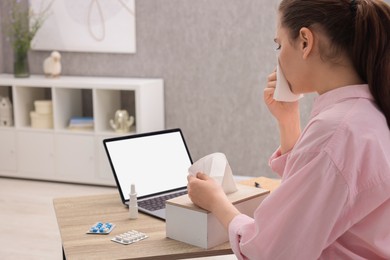 Sick woman having online consultation with doctor via laptop at wooden table indoors