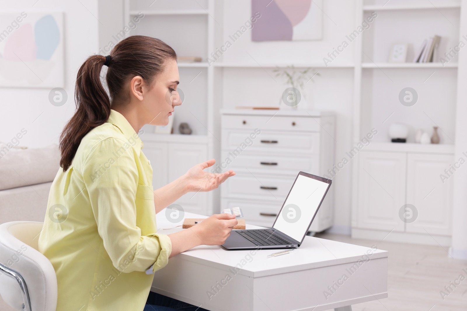 Photo of Sick woman with pills having online consultation with doctor via laptop at white table indoors