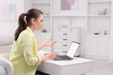 Sick woman with pills having online consultation with doctor via laptop at white table indoors