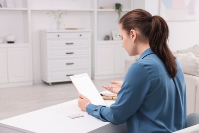 Sick woman having online consultation with doctor via tablet at white table indoors