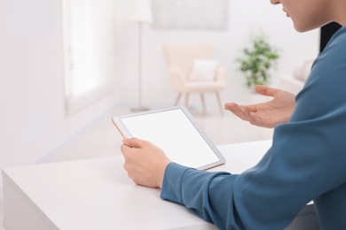 Sick woman having online consultation with doctor via tablet at white table indoors, closeup