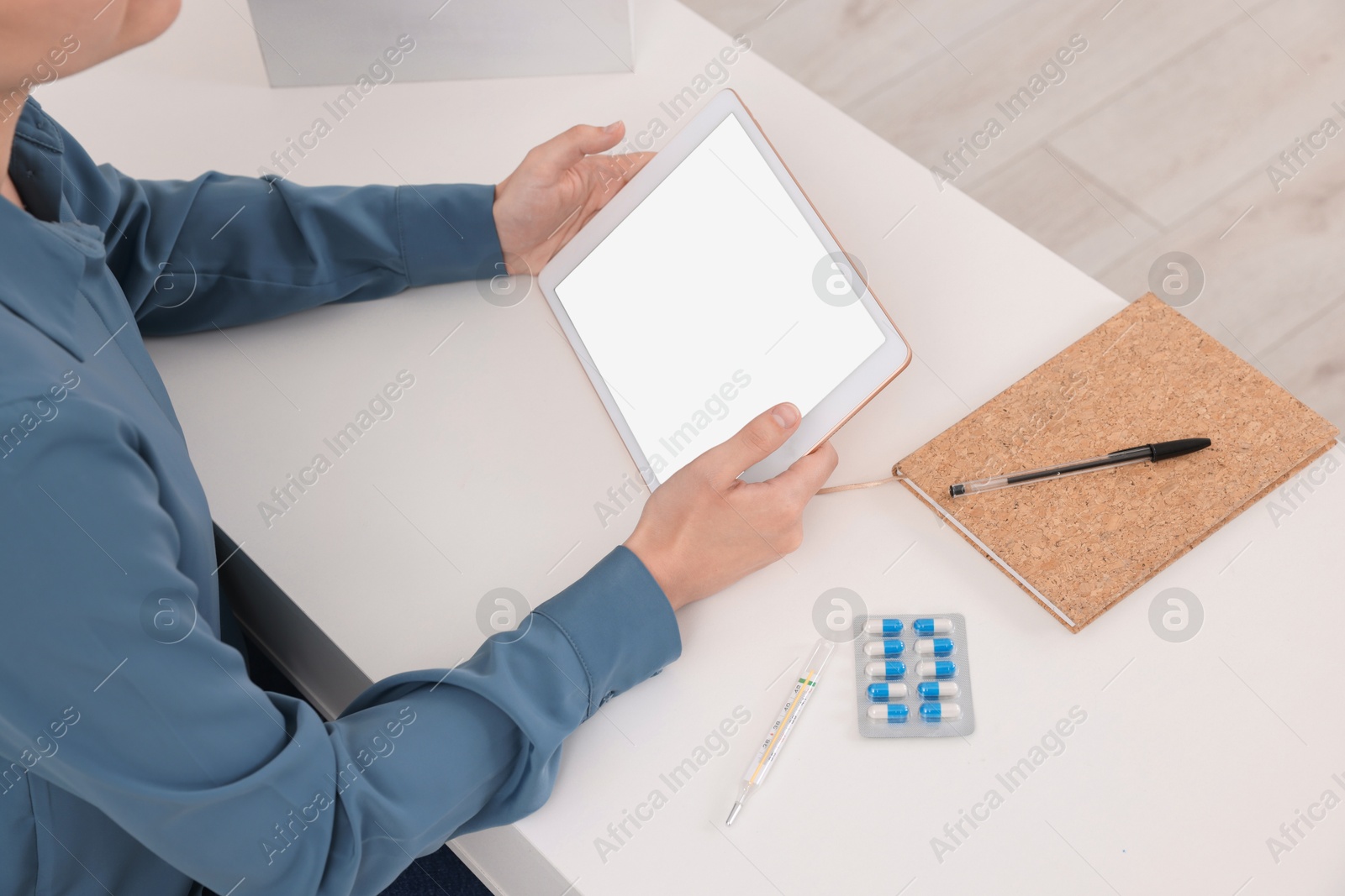 Photo of Sick woman having online consultation with doctor via tablet at white table indoors, closeup