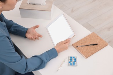 Sick woman having online consultation with doctor via tablet at white table indoors, closeup