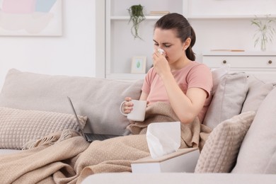 Sick woman with cup of tea having online consultation with doctor via laptop at home