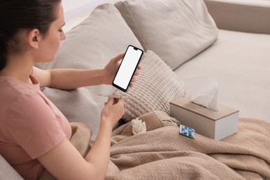 Sick woman with thermometer having online consultation with doctor via smartphone at home