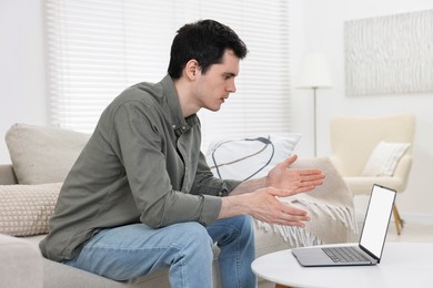 Sick man having online consultation with doctor via laptop at white table indoors