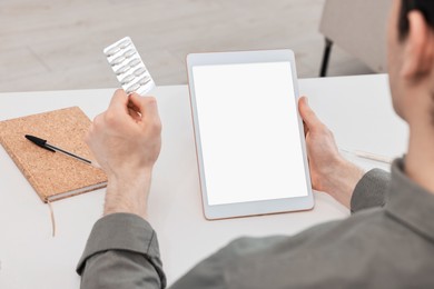 Sick man with pills having online consultation with doctor via tablet at white table indoors, closeup