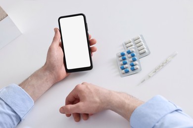 Photo of Sick man having online consultation with doctor via smartphone at white table indoors, closeup