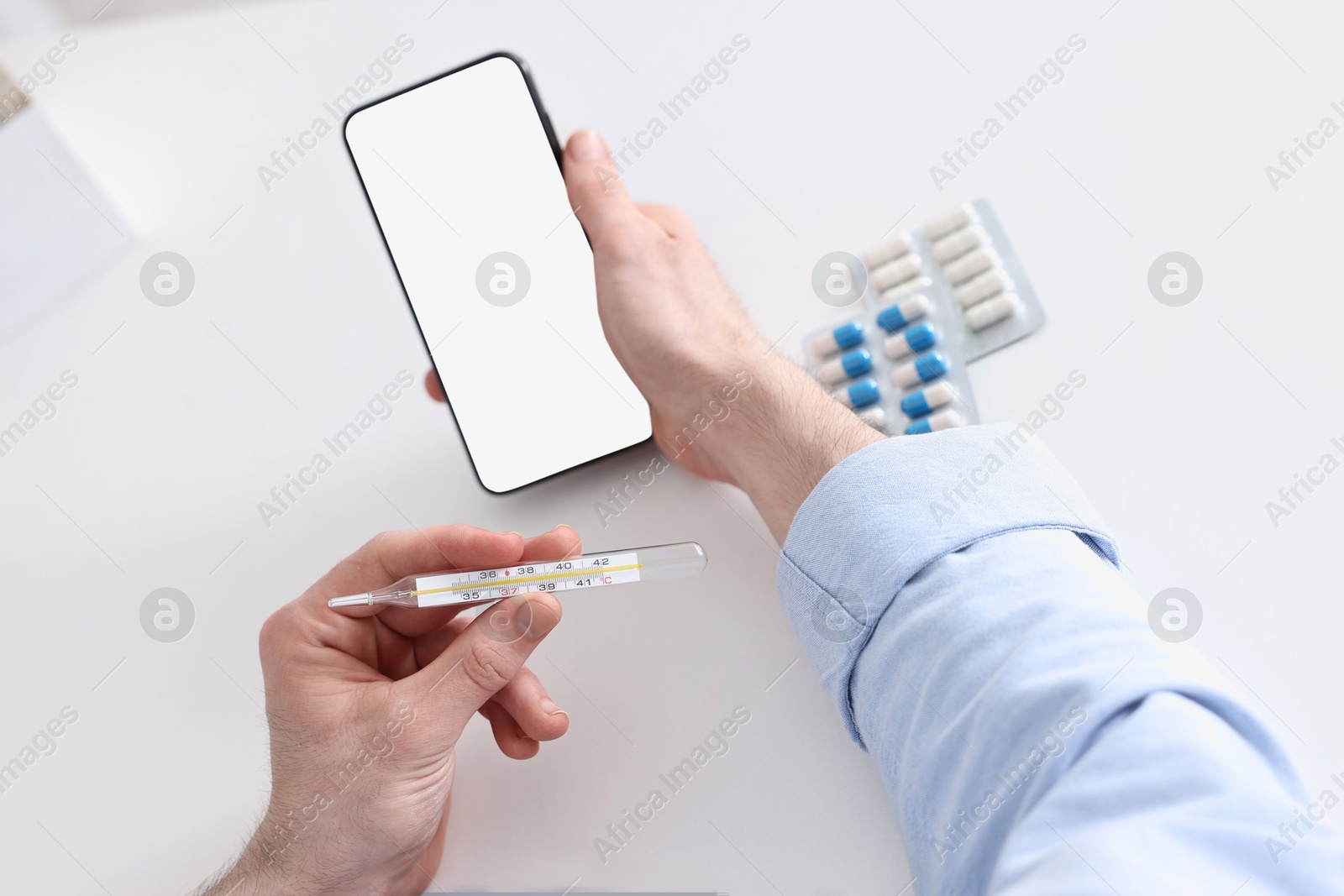 Photo of Sick man with thermometer having online consultation with doctor via smartphone at white table indoors, closeup