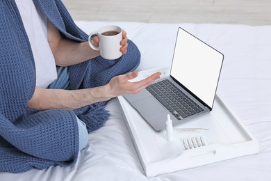 Photo of Sick man with of tea having online consultation with doctor via laptop at home, closeup