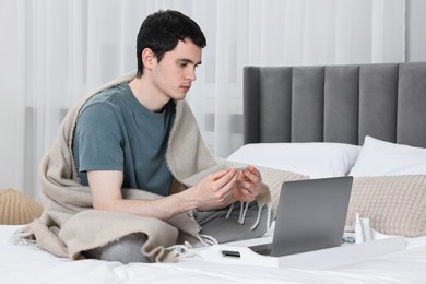 Photo of Sick man with thermometer having online consultation with doctor via laptop at home
