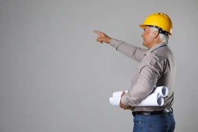 Engineer in hard hat with drafts on grey background, space for text