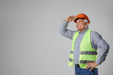 Engineer in hard hat on grey background, space for text