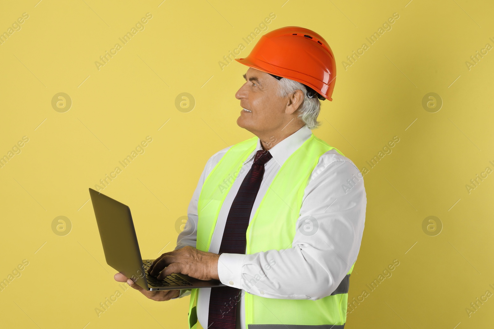 Photo of Engineer in hard hat with laptop on yellow background