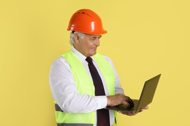 Photo of Engineer in hard hat with laptop on yellow background