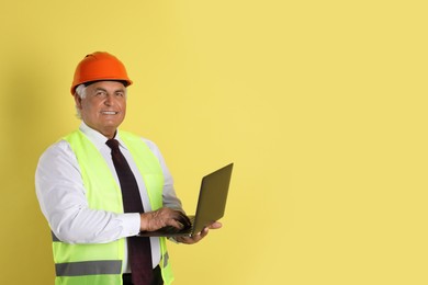 Photo of Engineer in hard hat with laptop on yellow background, space for text