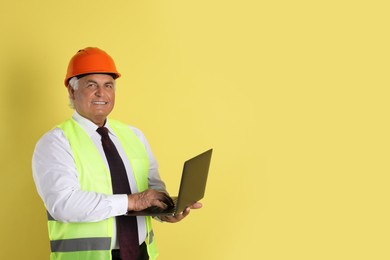 Engineer in hard hat with laptop on yellow background, space for text