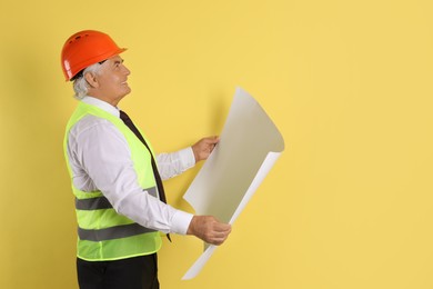 Engineer in hard hat with draft on yellow background, space for text