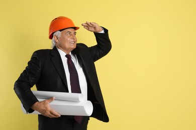 Photo of Engineer in hard hat with drafts on yellow background, space for text