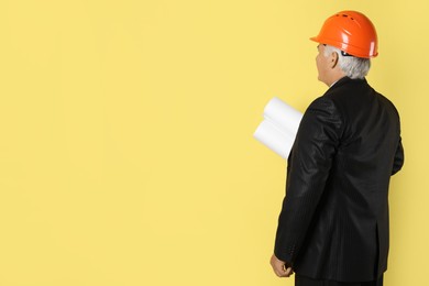 Photo of Engineer in hard hat with drafts on yellow background, space for text