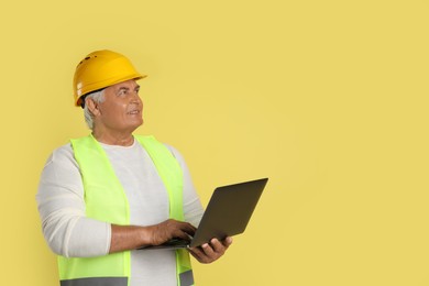 Engineer in hard hat with laptop on yellow background, space for text