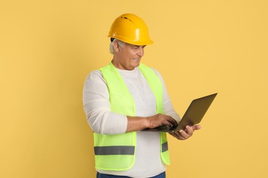 Engineer in hard hat with laptop on yellow background