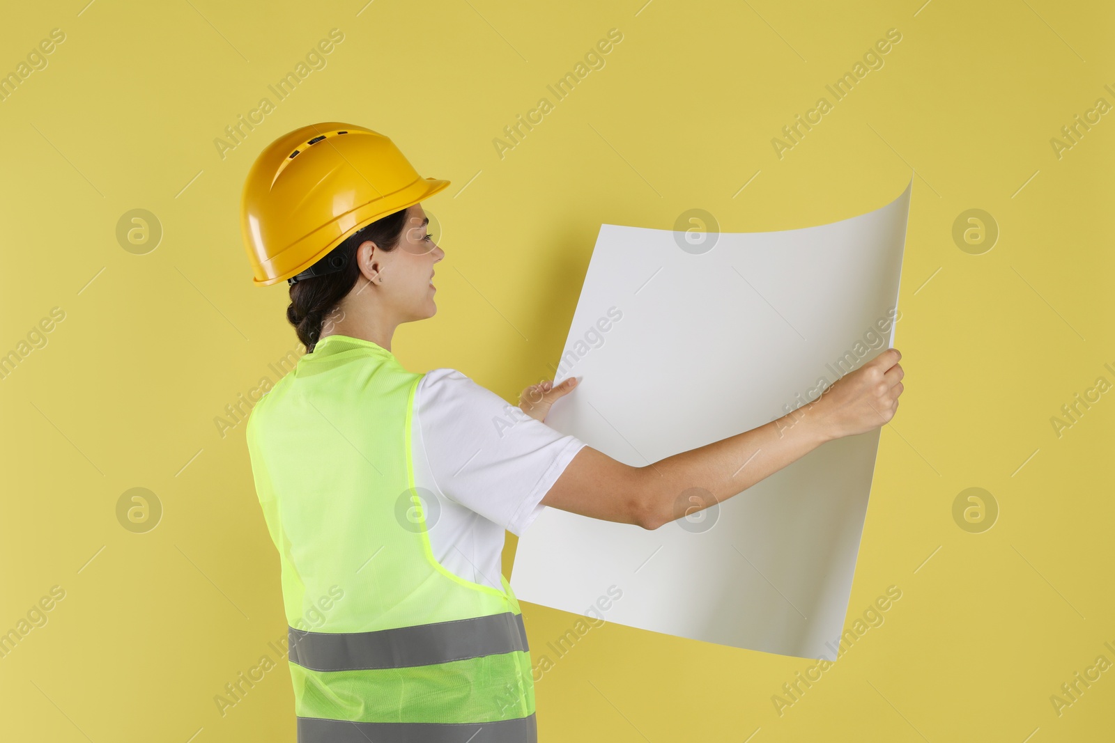 Photo of Engineer in hard hat with draft on yellow background