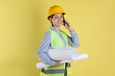 Photo of Engineer in hard hat with drafts talking on smartphone against yellow background