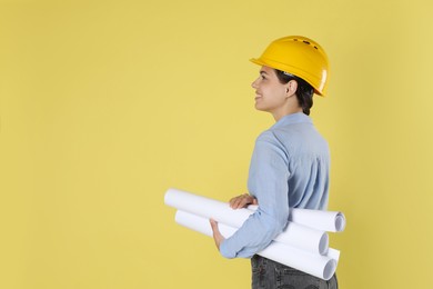 Photo of Engineer in hard hat with drafts on yellow background, space for text