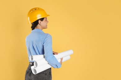 Photo of Engineer in hard hat with drafts on yellow background, space for text