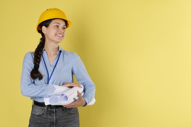 Photo of Engineer in hard hat with drafts on yellow background, space for text