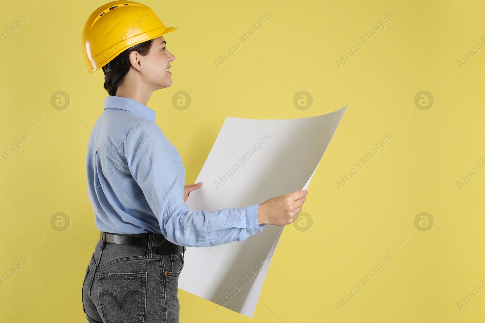 Photo of Engineer in hard hat with draft on yellow background, space for text